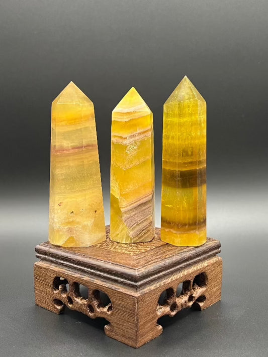 three yellow banded or lined fluorite points standing in a row on top of a craved square wooden stand